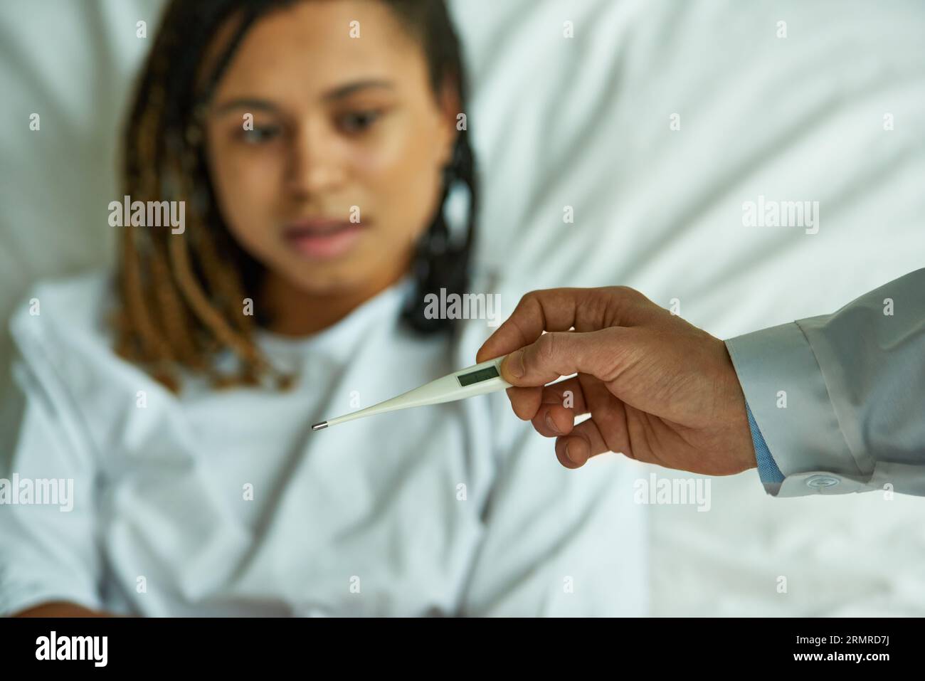 Arzt hält Thermometer in der Nähe von afroamerikanischer Frau, Privatstation, Krankenhaus, Symptome, Krankheit Stockfoto