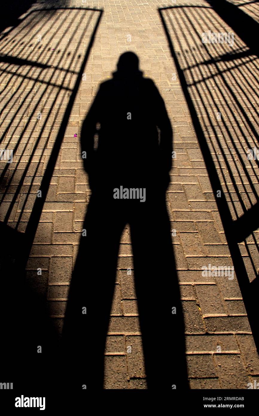 Voraussagender Schatten der Person, Beine auseinander, zwischen zwei halb offenen, schmiedeeisernen Toren stehend Stockfoto