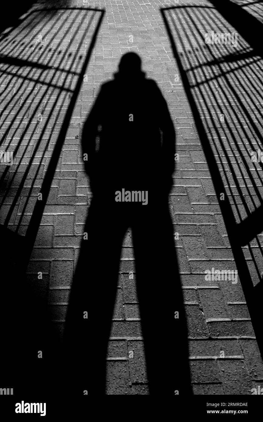 Voraussagender Schatten der Person, Beine auseinander, zwischen zwei halb offenen, schmiedeeisernen Toren stehend Stockfoto