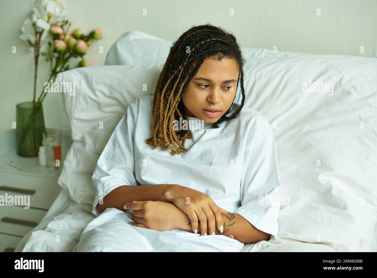 Verärgerte afroamerikanische Frau, die in der Privatstation liegt, Blumen, Glas Wasser, Krankenhaus, Fehlgeburt Stockfoto