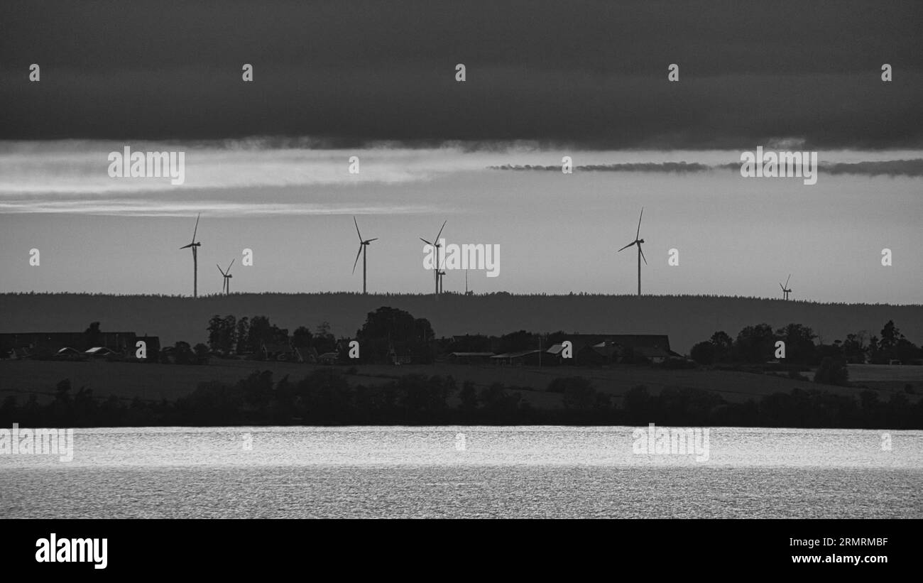 Windkraftanlagen, erneuerbare Energien, auf einem See bei Sonnenuntergang in Schwarz-weiß. Sauberer Strom für den Klimawandel. Bewölkter Himmel mit oranger Sonne in Scan Stockfoto