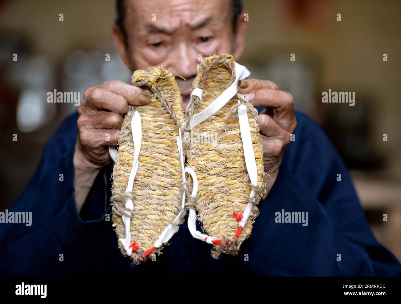 Chen Luoshou zeigt ein Paar Strohsandalen im Dorf Buqian in der Gemeinde Luoao im Yudu County in der ostchinesischen Provinz Jiangxi, 1. August 2014. Chen Luoshou, der 78 Jahre alt ist, ist einer der wenigen Handwerker, die Strohsandalen im Yudu County weben können. Obwohl heutzutage niemand Strohsandalen trägt, besteht der Septuagenist immer noch darauf, Strohsandalen jeden Tag zu weben. Ein Paar Strohsandalen kostet den alten Mann zwei Stunden und sie werden normalerweise mit 30 Yuan (4,85 US-Dollar) an Touristen oder Ausstellungshallen verkauft. (lfj) CHINA-JIANGXI-YUDU-STRAH SANDALENWEBER (CN) ChenxZixia PUBLICATIONx Stockfoto