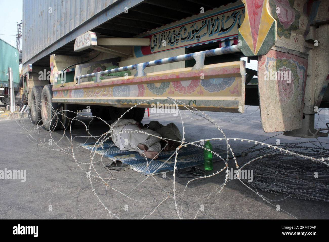 LAHORE, 7. August 2014 -- Ein Fahrer schläft unter einem Containerwagen, der von pakistanischer Polizei in der Nähe des Hauses des Religionsgelehrten Tahir-ul-Qadri die Straße blockiert, vor der bevorstehenden regierungsfeindlichen Kundgebung von Pakistan Awami Tehreek (PAT) im östlichen pakistanischen Lahore am 7. August 2014. Tahir-ul-Qadri hat eine Kampagne gegen Nawaz Sharif gestartet und hat angedeutet, Khans langem marsch beizutreten. Die Bedrohung durch einen landesweiten Protest der Tehrik-e-Insaf unter der Führung des Cricketkünstlers Imran Khan hat die Regierung des pakistanischen Premierministers Nawaz Sharif unter Druck gesetzt. PAKISTAN-LAHORE-PROTEST JAMILXAHMED PUBL Stockfoto