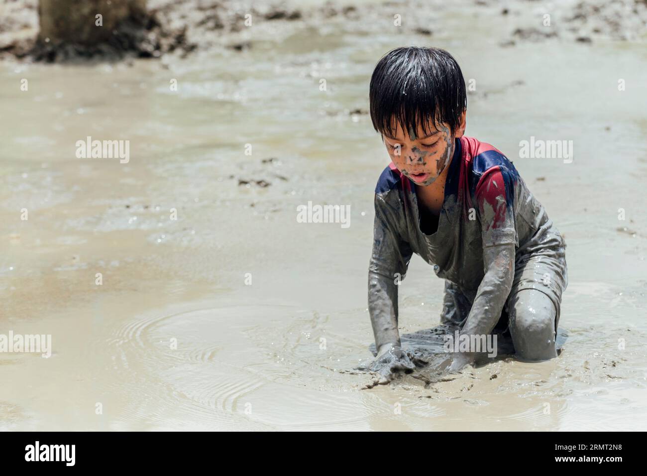 Süßer, glücklicher kleiner asiatischer Junge, der gerne im Schlamm auf dem Spielplatz spielt. Kindererziehung in der Natur an der montessori-Schule. Natur- und Bildungskonzept. Stockfoto