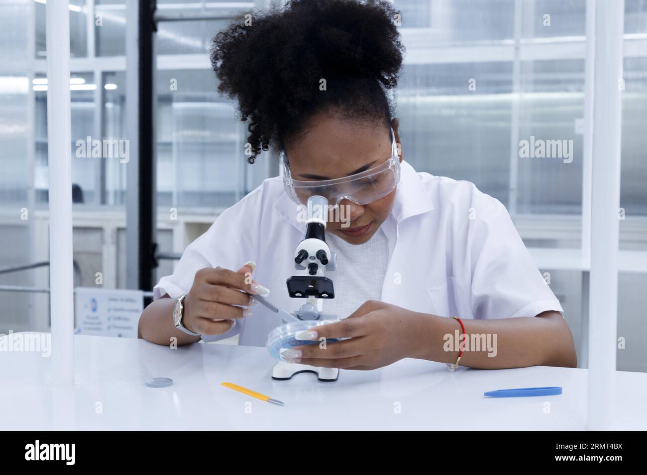 Afrikanische Ärztin Studentin Wissenschaftlerin mit Blick auf das Mikroskop analysiert Virentestprobe. Junger Biotechnologie-Spezialist im Labor. Medizinische Wissenschaft Stockfoto