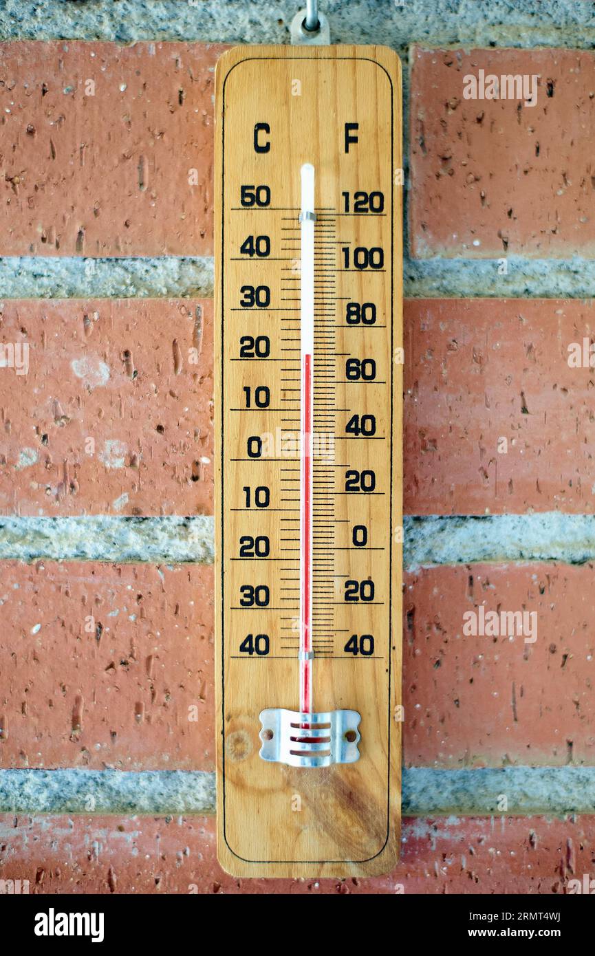 Thermometer an Ziegelwand: Messbilder in rustikaler Umgebung. Details eines Holzfußthermometers an einer braunen Ziegelwand, das die Temperatur anzeigt Stockfoto