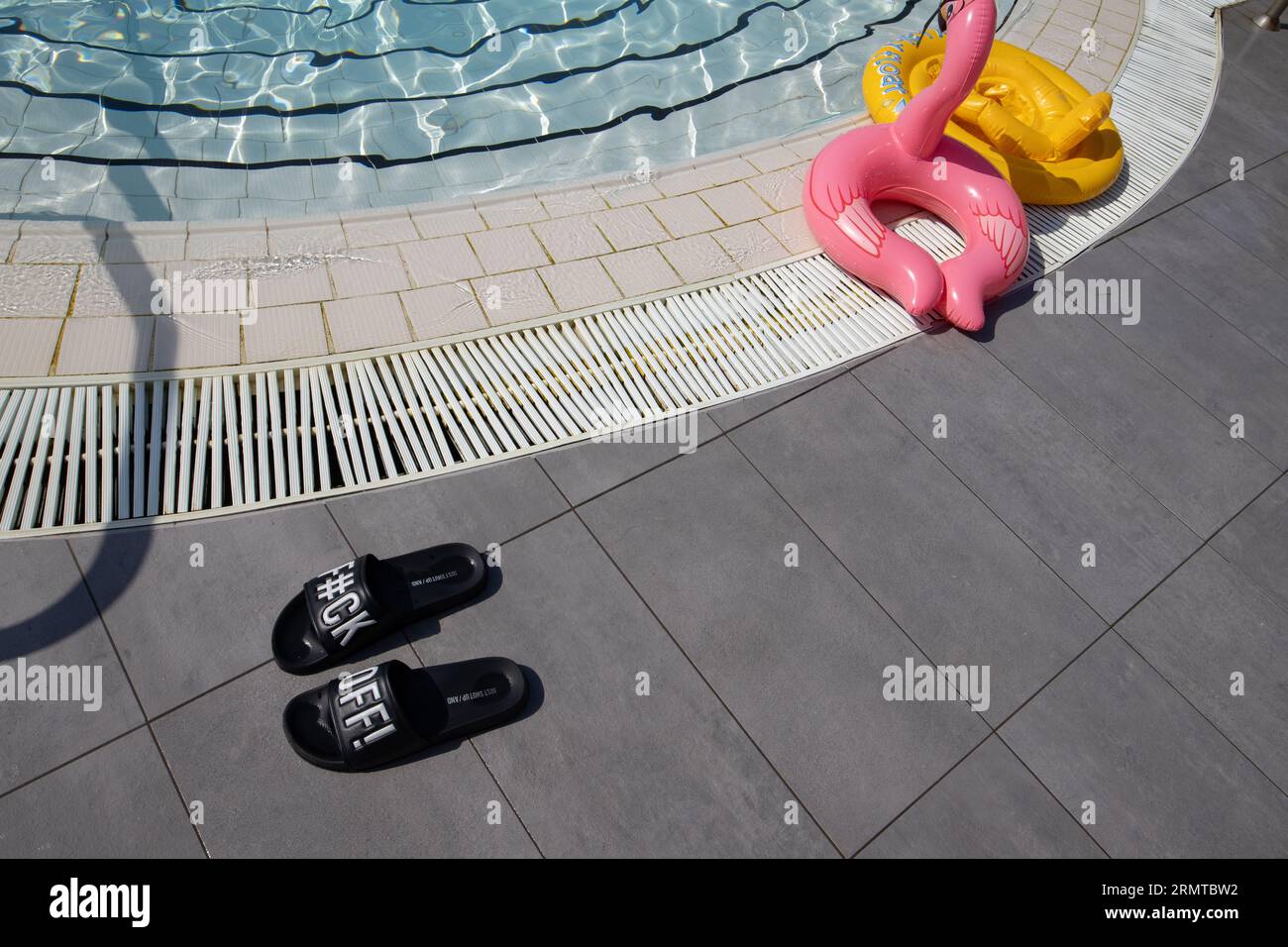 Sandalen am Pool mit einer unverwechselbaren unhöflichen Botschaft, die neben einem Swimmingpool in einem europäischen Ferienort hinterlassen wird, köcheln 2023 Stockfoto