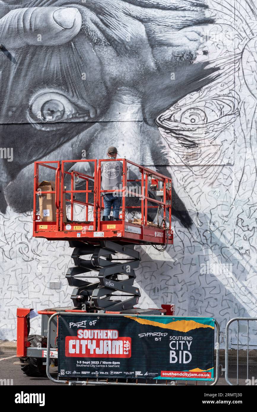 Southend on Sea, Essex, Großbritannien. 30. August 2023. Southend, das als Europas größtes Street-Art-Festival bezeichnet wird, feiert mit dem City Jam-Event seinen neuen Stadtstatus weiter. Über 200 lokale, nationale und internationale Straßenkünstler zeigen ihre Fähigkeiten an 100 Orten im Stadtzentrum. Einige provisorische Mauern wurden errichtet, aber die Künstler schmücken auch die Seiten von Gebäuden und andere dauerhafte Strukturen. Vom ersten bis zum dritten September haben die Künstler mit der Arbeit an den größeren Wandgemälden begonnen, um für die Veranstaltung bereit zu sein. Männlicher Künstler, der an grossen Fototapeten arbeitet Stockfoto