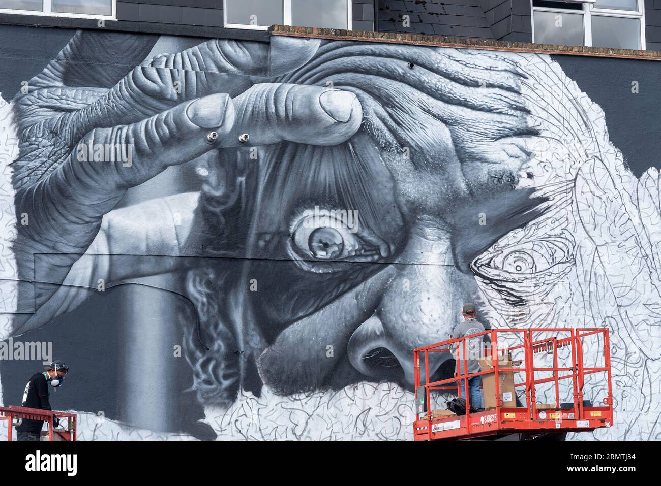 Southend on Sea, Essex, Großbritannien. 30. August 2023. Southend, das als Europas größtes Street-Art-Festival bezeichnet wird, feiert mit dem City Jam-Event seinen neuen Stadtstatus weiter. Über 200 lokale, nationale und internationale Straßenkünstler zeigen ihre Fähigkeiten an 100 Orten im Stadtzentrum. Einige provisorische Mauern wurden errichtet, aber die Künstler schmücken auch die Seiten von Gebäuden und andere dauerhafte Strukturen. Vom ersten bis zum dritten September haben die Künstler mit der Arbeit an den größeren Wandgemälden begonnen, um für die Veranstaltung bereit zu sein. Männlicher Künstler, der an grossen Fototapeten arbeitet Stockfoto