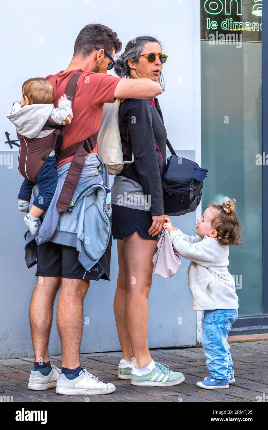 Familie mit kleinen Kindern, die ihre Rucksäcke in der City Center Street anpassen - Tours, Indre-et-Loire (37), Frankreich. Stockfoto