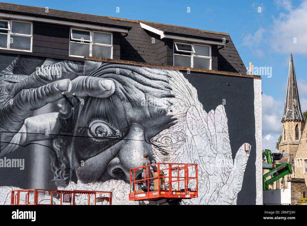 Southend on Sea, Essex, Großbritannien. 30. August 2023. Southend, das als Europas größtes Street-Art-Festival bezeichnet wird, feiert mit dem City Jam-Event seinen neuen Stadtstatus weiter. Über 200 lokale, nationale und internationale Straßenkünstler zeigen ihre Fähigkeiten an 100 Orten im Stadtzentrum. Einige provisorische Mauern wurden errichtet, aber die Künstler schmücken auch die Seiten von Gebäuden und andere dauerhafte Strukturen. Vom ersten bis zum dritten September haben die Künstler mit der Arbeit an den größeren Wandgemälden begonnen, um für die Veranstaltung bereit zu sein. Männlicher Künstler, der an grossen Fototapeten arbeitet Stockfoto