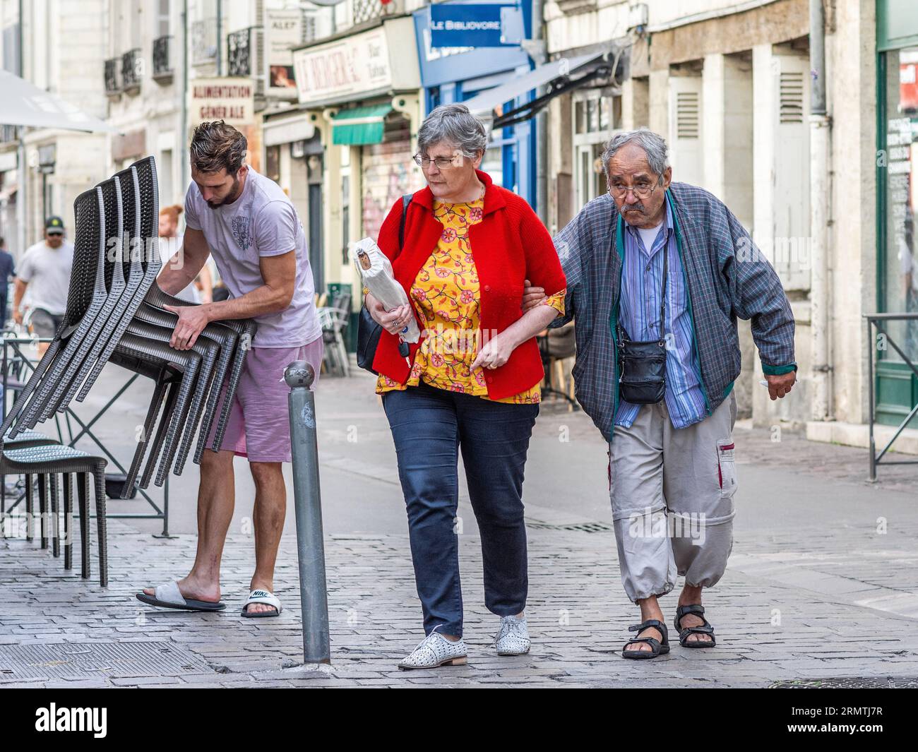 Älteres Paar, das auf der Kopfsteinpflasterstraße spaziert, mit stapelbaren Stühlen des Café-Barkeepers - Tours, Indre-et-Loire (37), Frankreich. Stockfoto