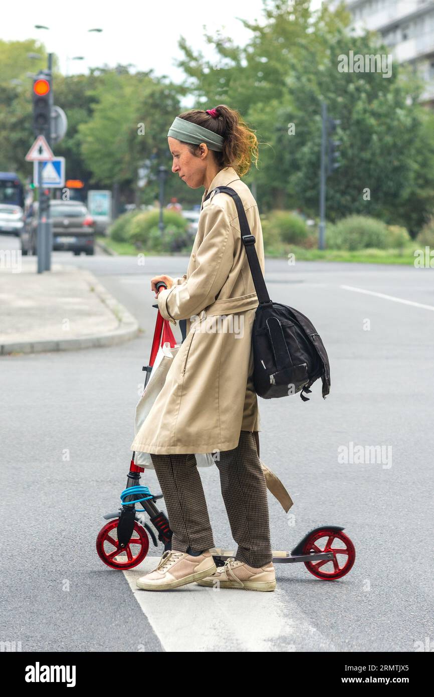 Junge Frau, die den Roller über die Straße schiebt - Tours, Indre-et-Loire (37), Frankreich. Stockfoto