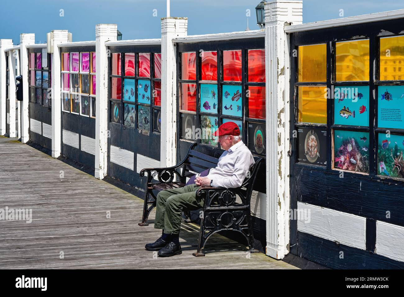 Ein elegant gekleideter älterer Gentleman in roter Mütze, der einen Sommertag am Worthing Pier im Westen von Sussex, England, genießt Stockfoto