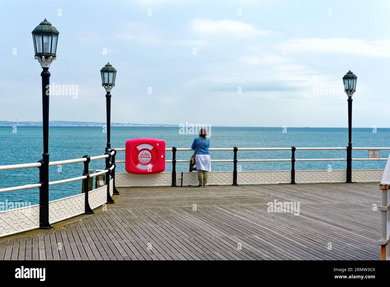 Eine einsame weibliche Figur, die am Ende des Worthing Pier an einem klaren Sommertag in Worthing West Sussex England auf das Meer blickt Stockfoto