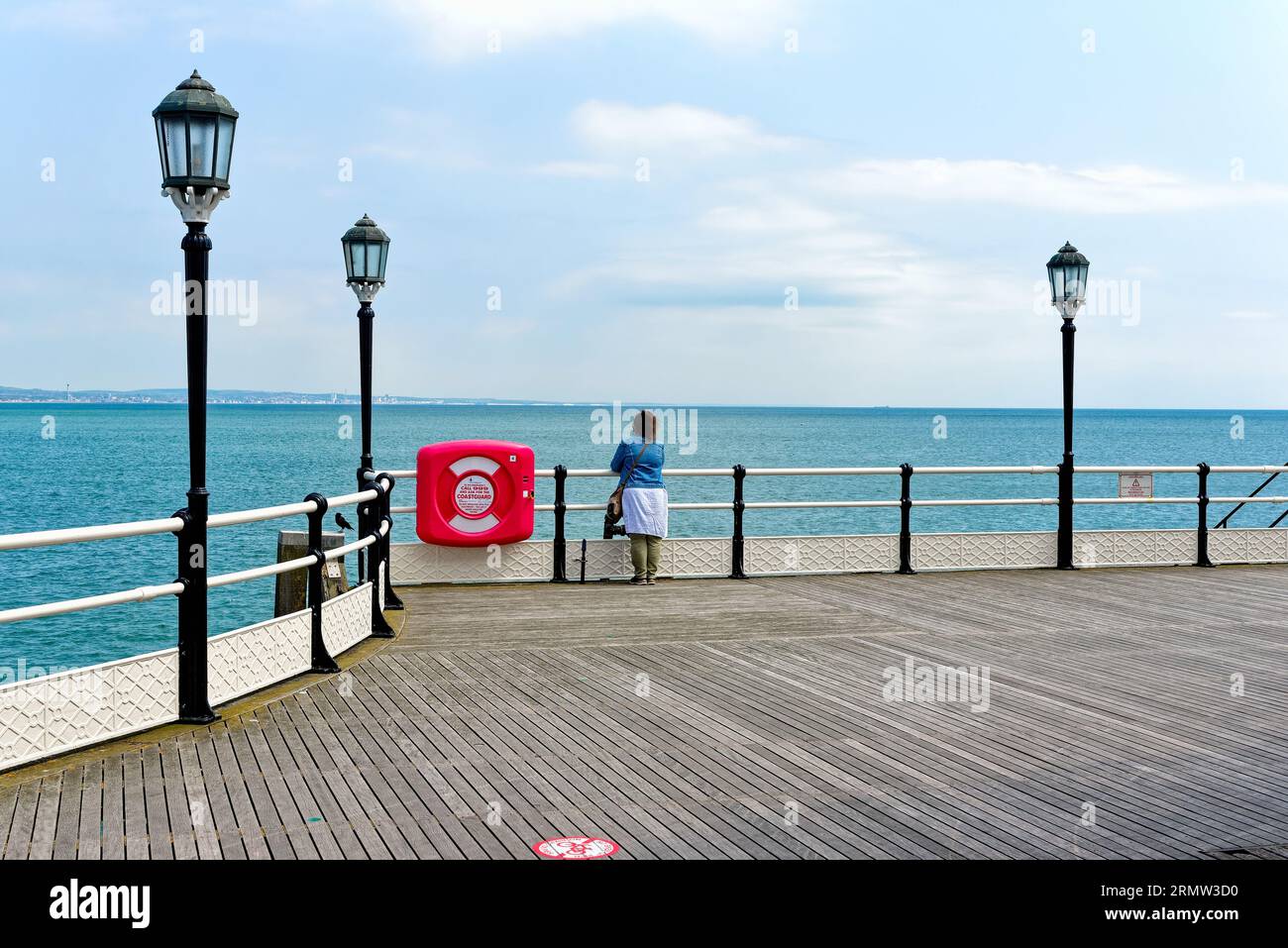 Eine einsame weibliche Figur, die am Ende des Worthing Pier an einem klaren Sommertag in Worthing West Sussex England auf das Meer blickt Stockfoto