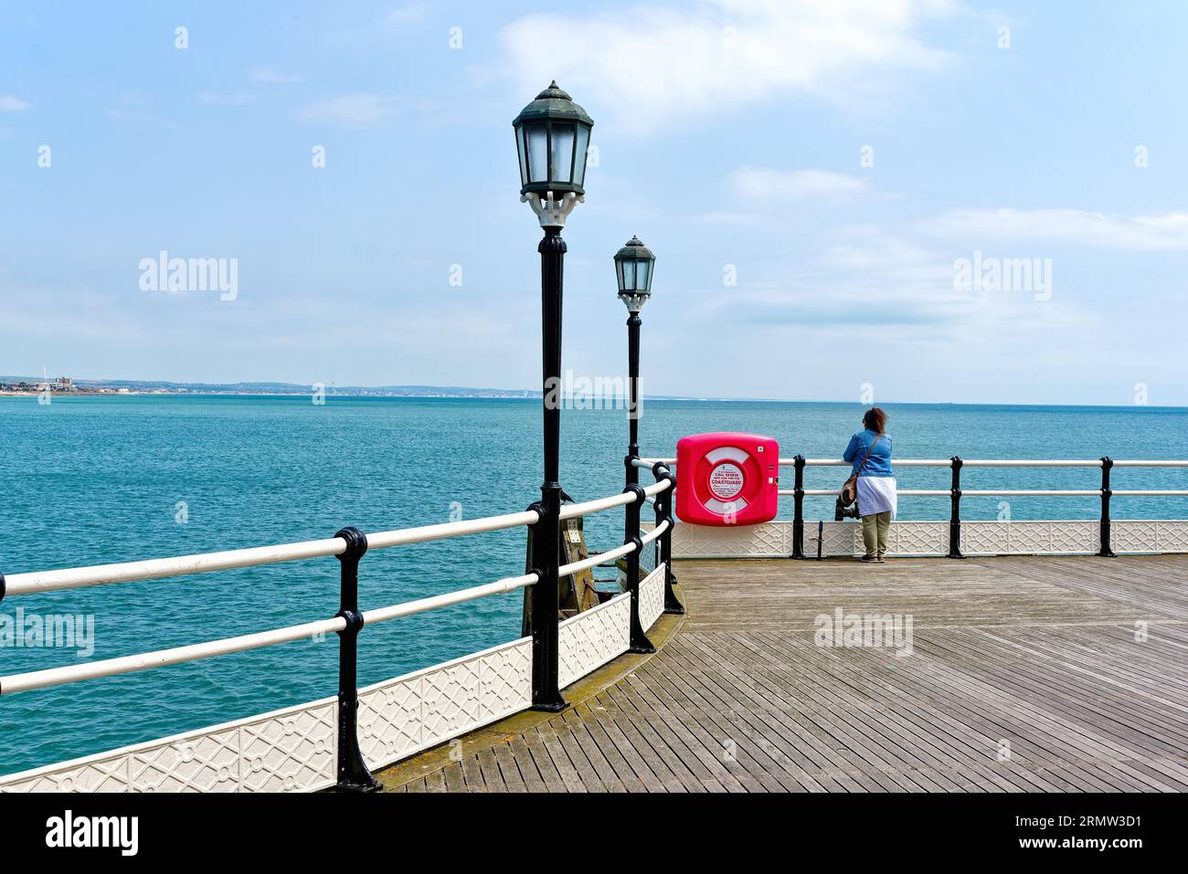 Eine einsame weibliche Figur, die am Ende des Worthing Pier an einem klaren Sommertag in Worthing West Sussex England auf das Meer blickt Stockfoto
