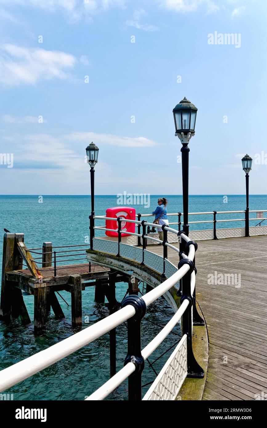 Eine einsame weibliche Figur, die am Ende des Worthing Pier an einem klaren Sommertag in Worthing West Sussex England auf das Meer blickt Stockfoto
