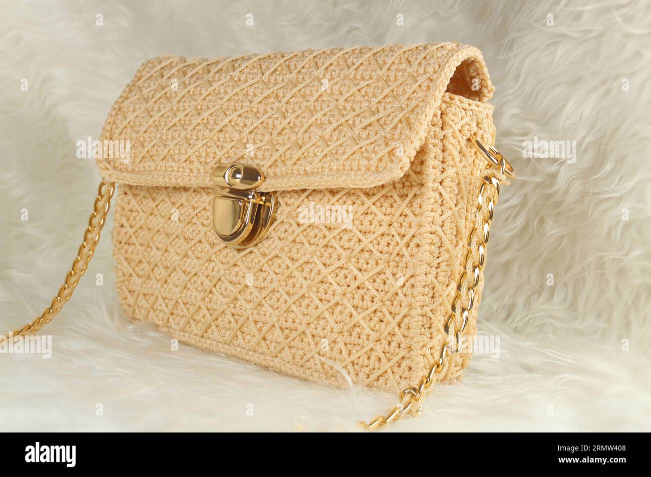 Gestrickte, handgemachte, hellbeige Tasche auf einer weißen Pelzdecke. Stockfoto