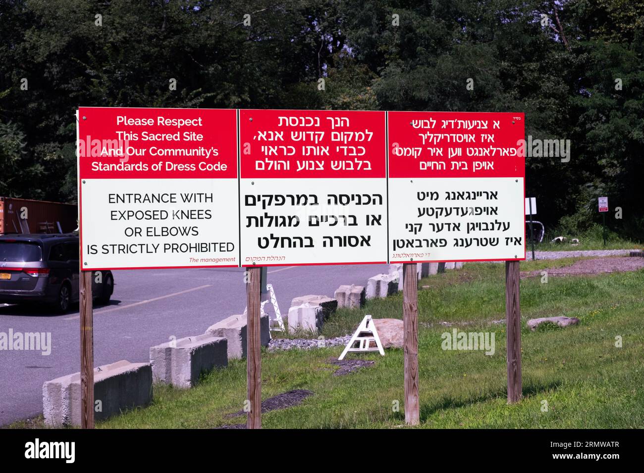 Ein Schild auf einem orthodoxen jüdischen Friedhof in drei Sprachen, das Frauen zwingt, sich bescheiden zu kleiden. Stockfoto