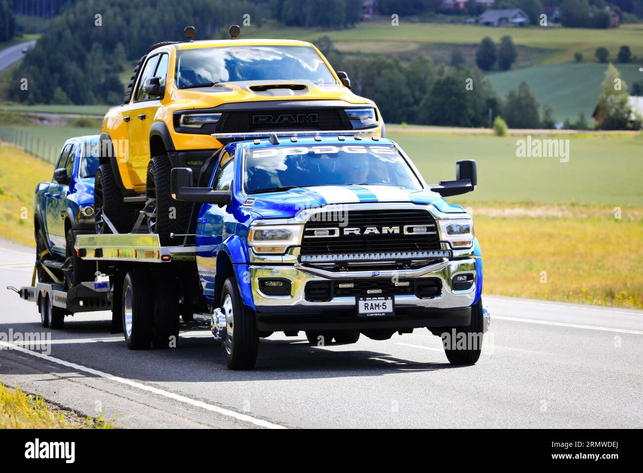 Der leistungsstarke und maßgeschneiderte RAM 5500-Lkw transportiert zwei Pickup-Lkw, einen gelben RAM und einen 3. Leichten Lkw auf Anhänger. Highway 3, Finnland. August 2023. Stockfoto