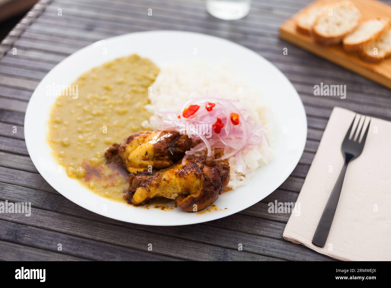 Peruanisches Gericht. Hähnchenflügel mit Erbsenpüree, Reis und eingelegten Zwiebeln Stockfoto