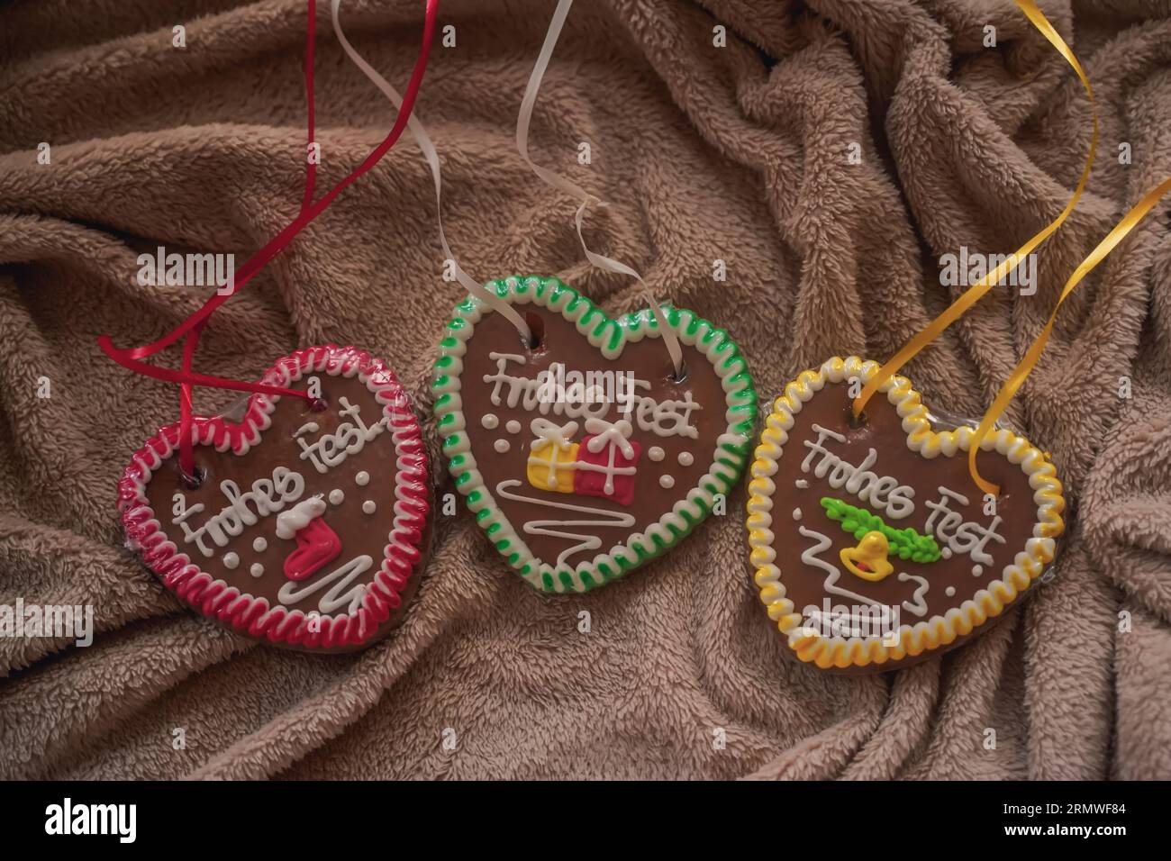 Rote, grüne, gelbe Lebkuchen mit buntem Creme und Band liegen auf braunem Stoffhintergrund aus nächster Nähe von oben Stockfoto