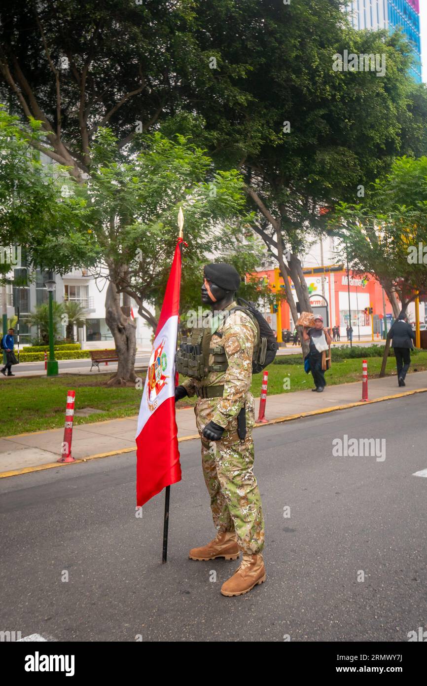 Lima, Peru - Juli 29 2023: Junger peruanischer Mann mit schwarzer und oranger Gesichtsfarbe, trägt Tarnkleidung und eine kugelsichere Weste, hält eine Flagge in Th Stockfoto