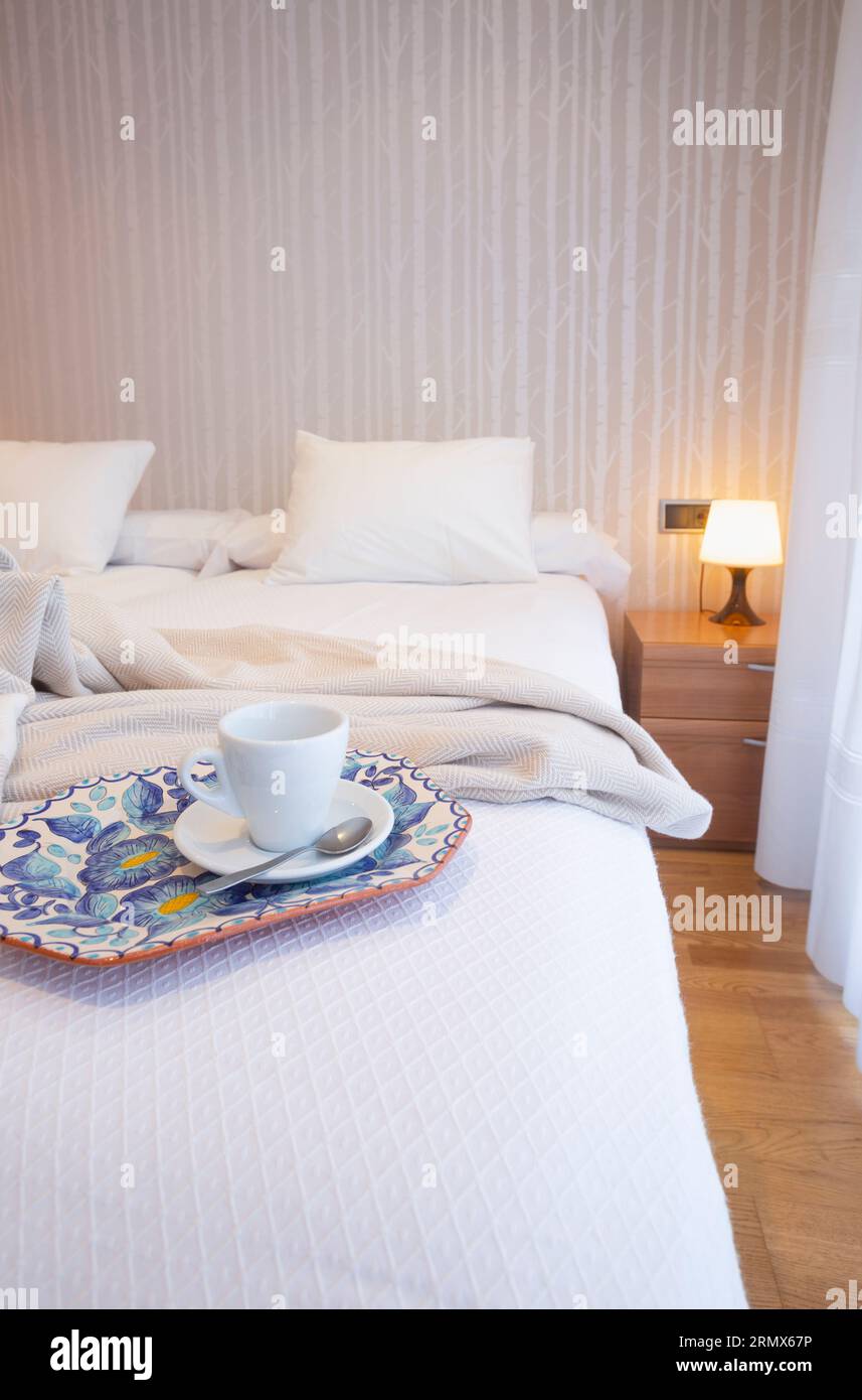 Schlafzimmer mit weißem Bett, Bambustapete, grauem Schal, Kaffeetasse und Tablett mit Blumen dekoriert. Stockfoto