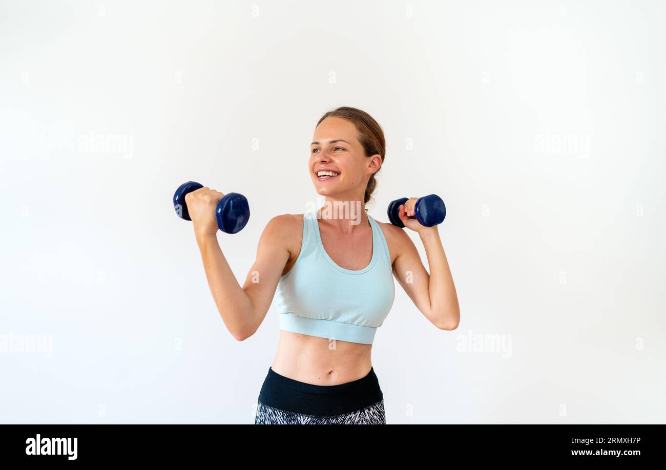Sportlifestyle weibliche Athletin posiert mit Kurzhanteln in den Händen vor weißem Hintergrund im Studio und lächelt. Stockfoto