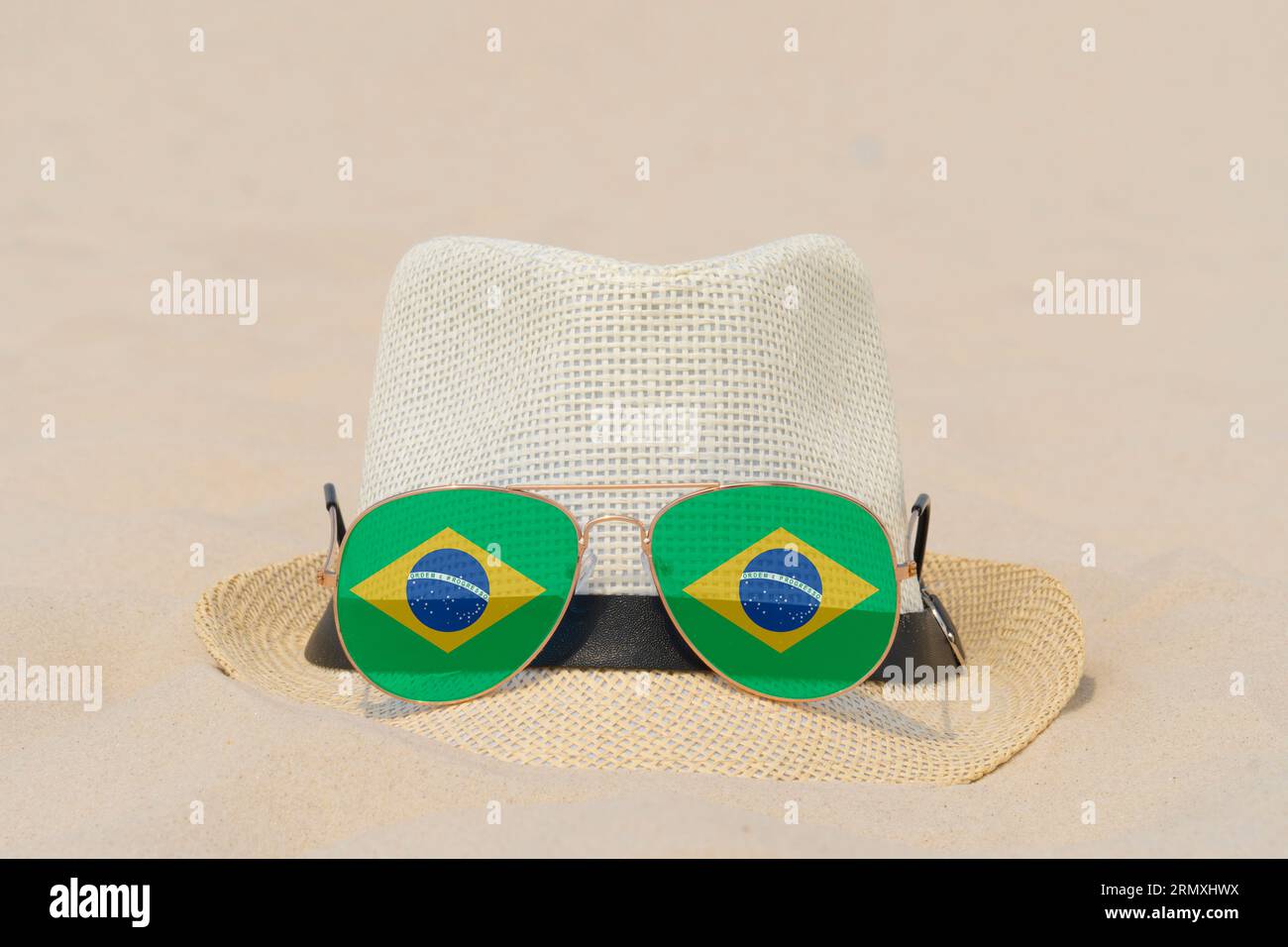 Sonnenbrille mit Brille in Form einer brasilianischen Flagge und einem Hut liegen auf Sand. Konzept von Sommerferien und Reisen in Brasilien. Sommerruhe. Weihnachtszeit Stockfoto