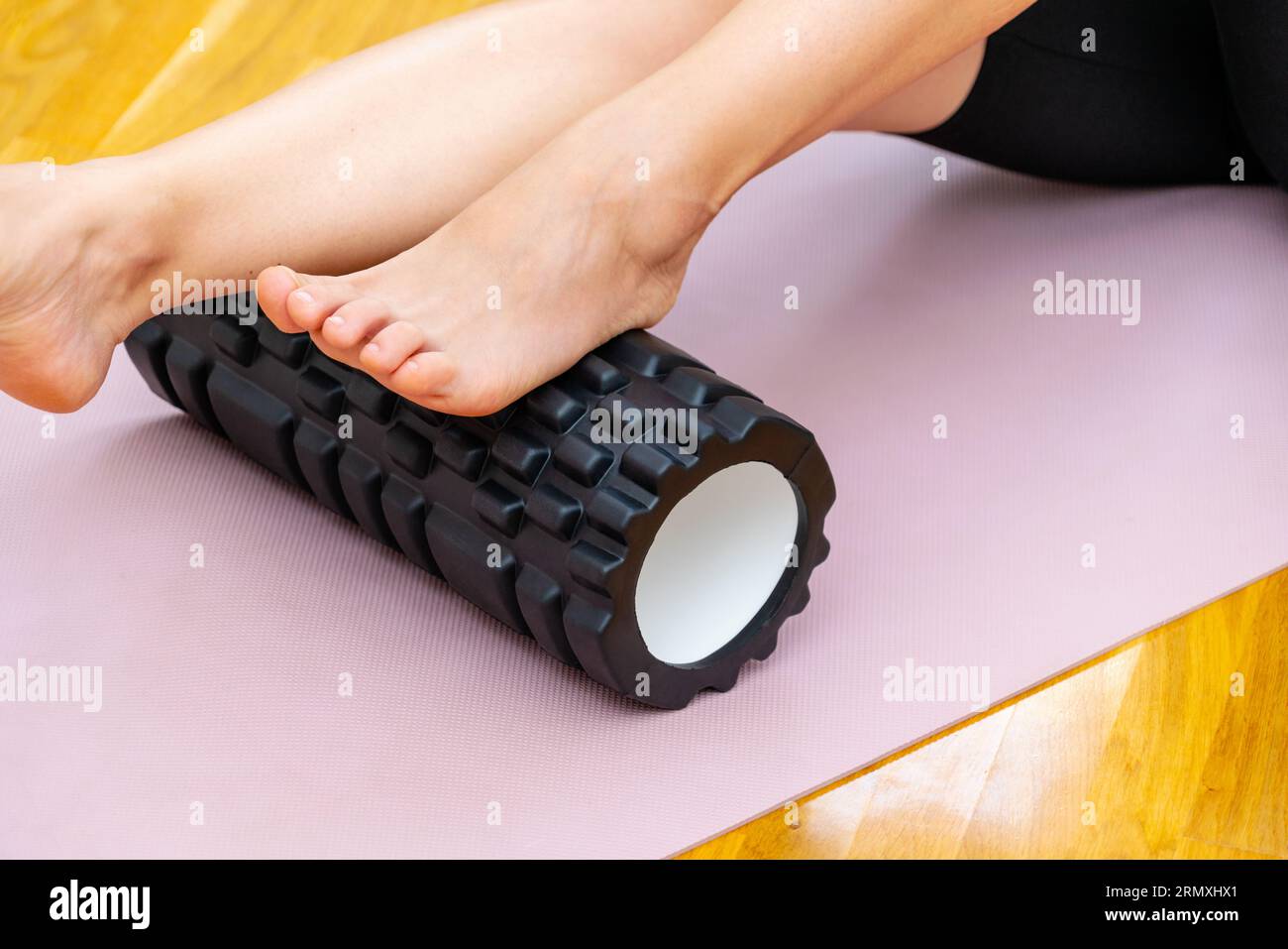 Mit Schaumstoffrolle zur Selbstmassage der Füße. Nahaufnahme von Fitnessroller und weiblichem Fuß. Stockfoto