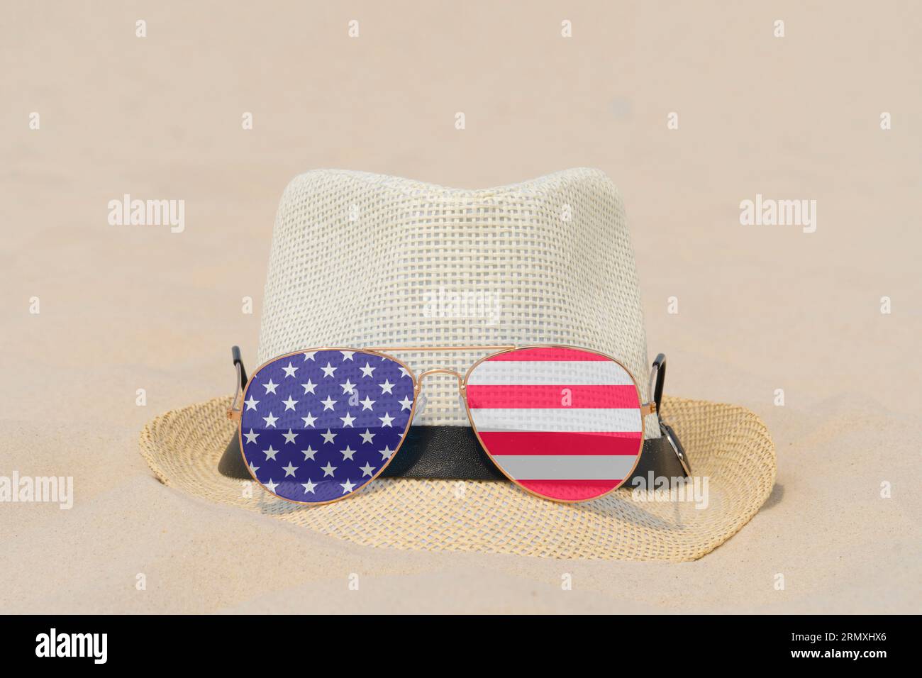 Sonnenbrille mit Brille in Form einer Flagge der USA und einem Hut liegen auf Sand. Konzept von Sommerferien und Reisen in den USA. Sommerruhe. Weihnachtszeit Stockfoto