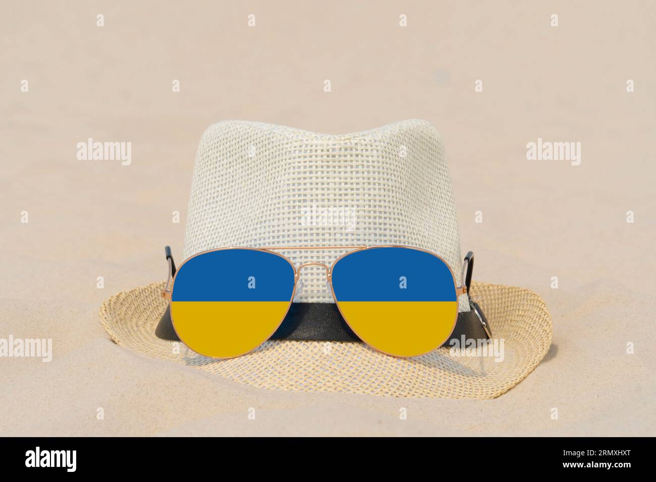 Sonnenbrillen mit Gläsern in Form einer Flagge der Ukraine und einem Hut liegen auf Sand. Konzept von Sommerferien und Reisen in der Ukraine. Sommerruhe Stockfoto