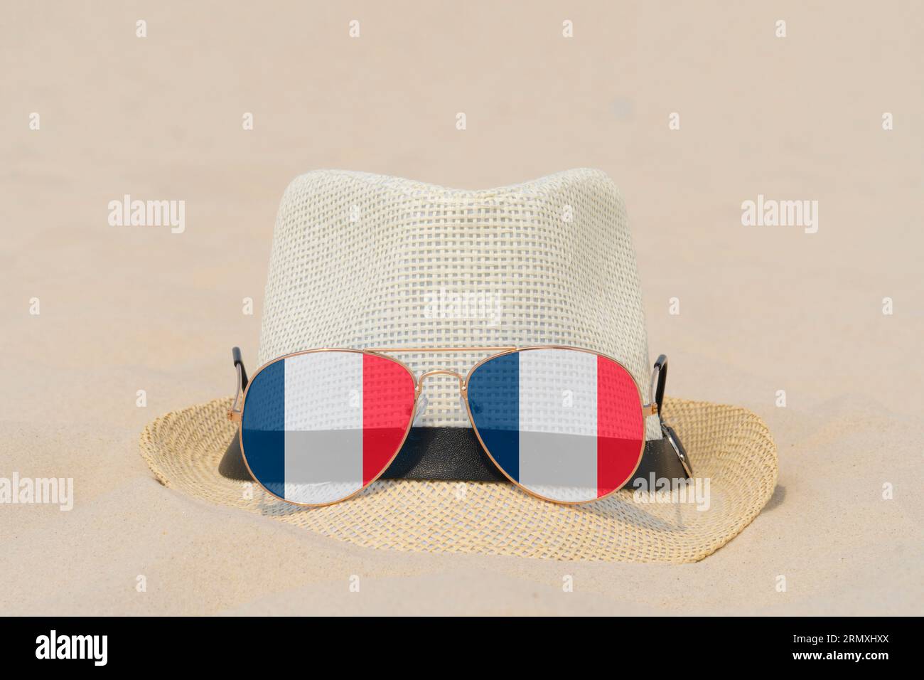 Sonnenbrille mit Gläsern in Form einer französischen Flagge und einem Hut liegen auf Sand. Konzept der Sommerferien und Reisen in Frankreich. Sommerruhe. Weihnachtszeit Stockfoto