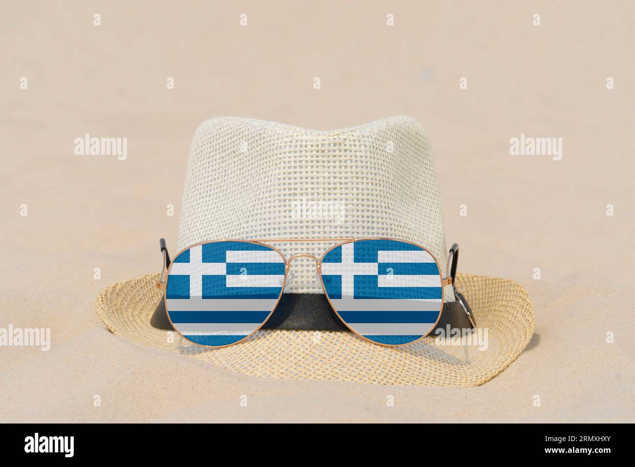 Sonnenbrillen mit Gläsern in Form einer griechischen Flagge und einem Hut liegen auf Sand. Konzept von Sommerferien und Reisen in Griechenland. Sommerruhe. Weihnachtszeit Stockfoto