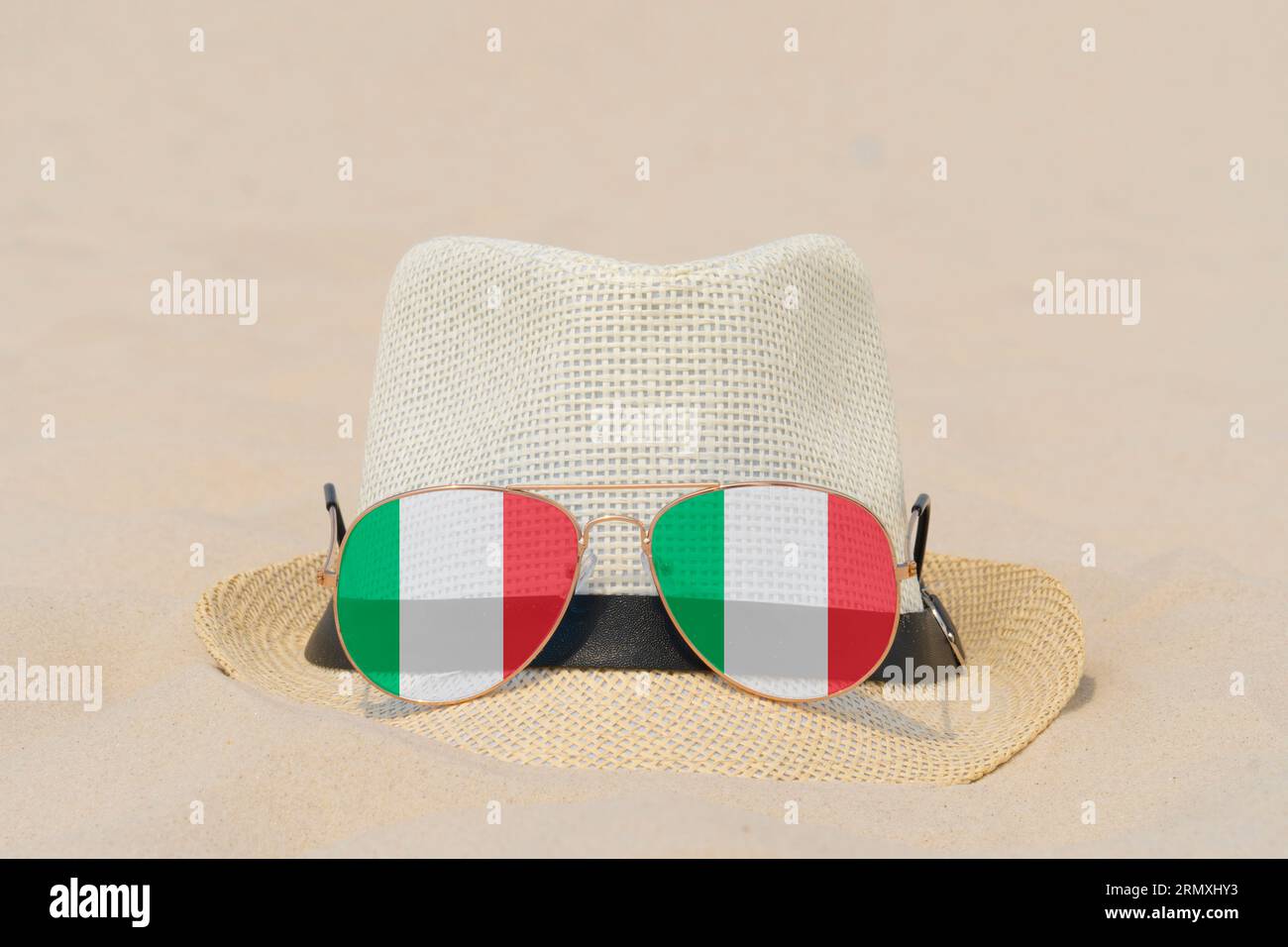 Sonnenbrille mit Gläsern in Form einer italienischen Flagge und einem Hut liegen auf Sand. Konzept der Sommerferien und Reisen in Italien. Sommerruhe. Weihnachtszeit Stockfoto