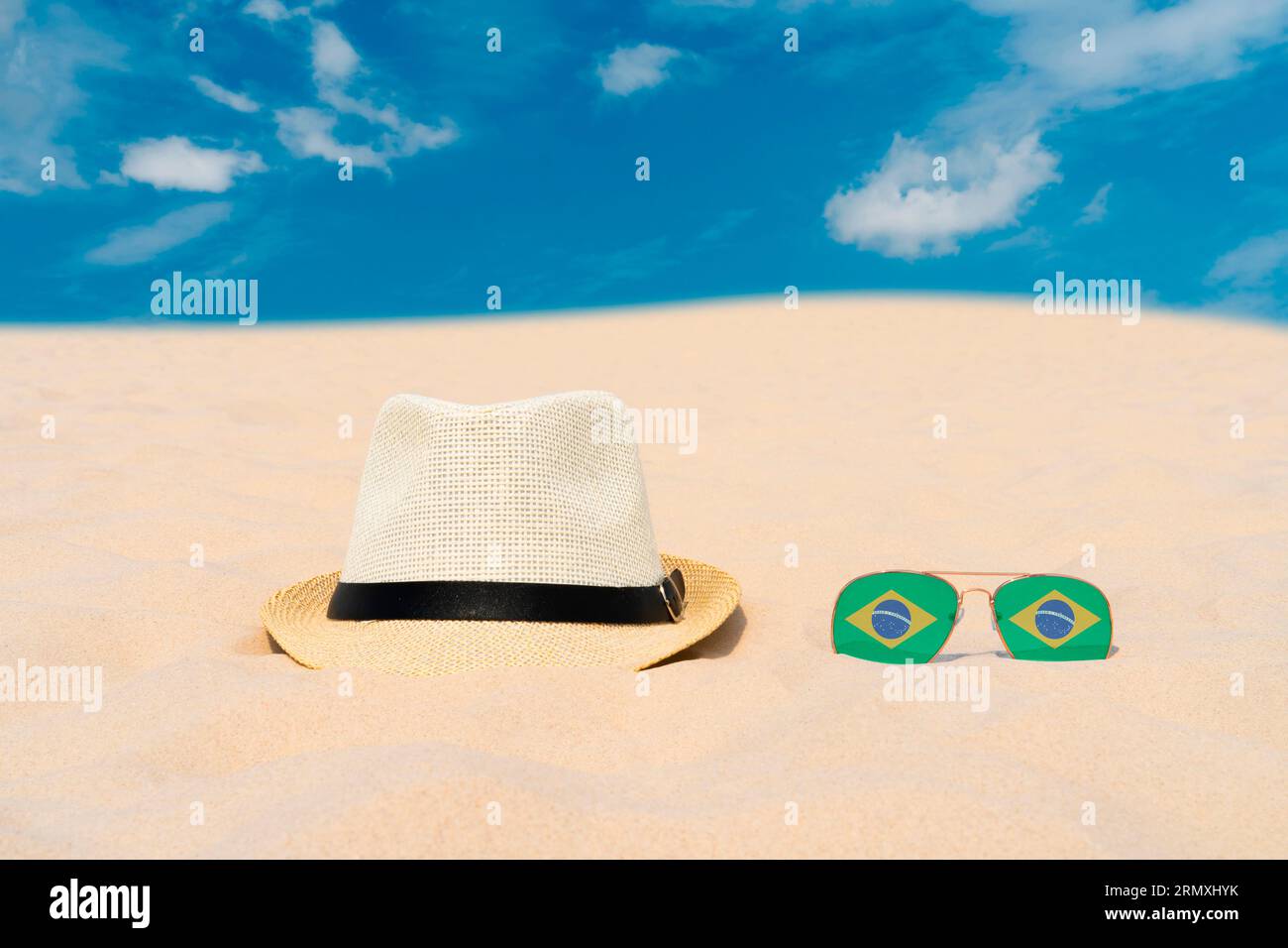 Sonnenbrille mit Brille in Form einer brasilianischen Flagge und einem Hut liegen auf Sand vor blauem Himmel. Konzept von Sommerferien und Reisen in Brasilien. Sommerruhe Stockfoto