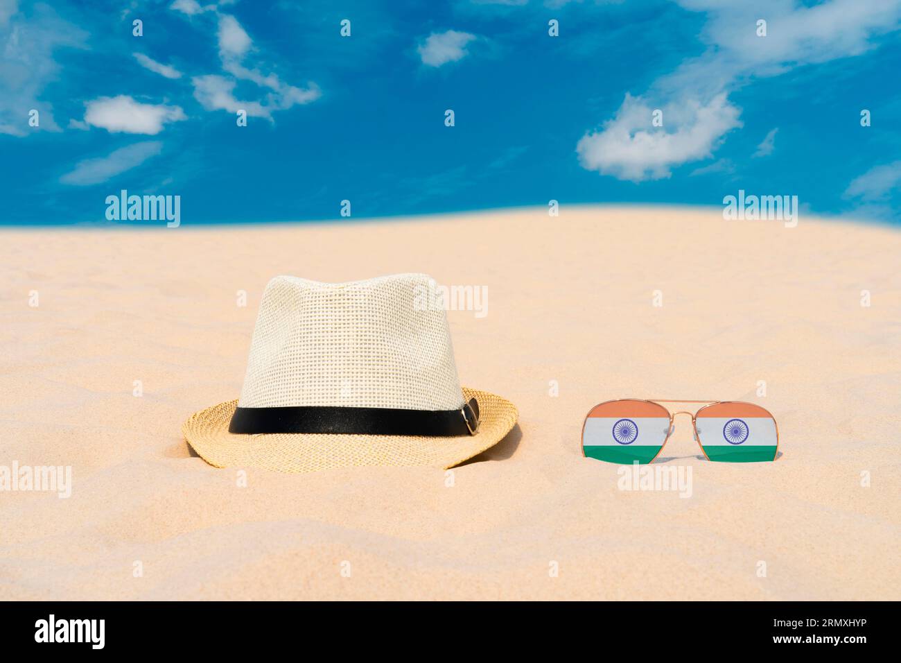 Sonnenbrillen mit Gläsern in Form einer indischen Flagge und einem Hut liegen auf Sand gegen blauen Himmel. Konzept von Sommerferien und Reisen in Indien. Sommerruhe Stockfoto