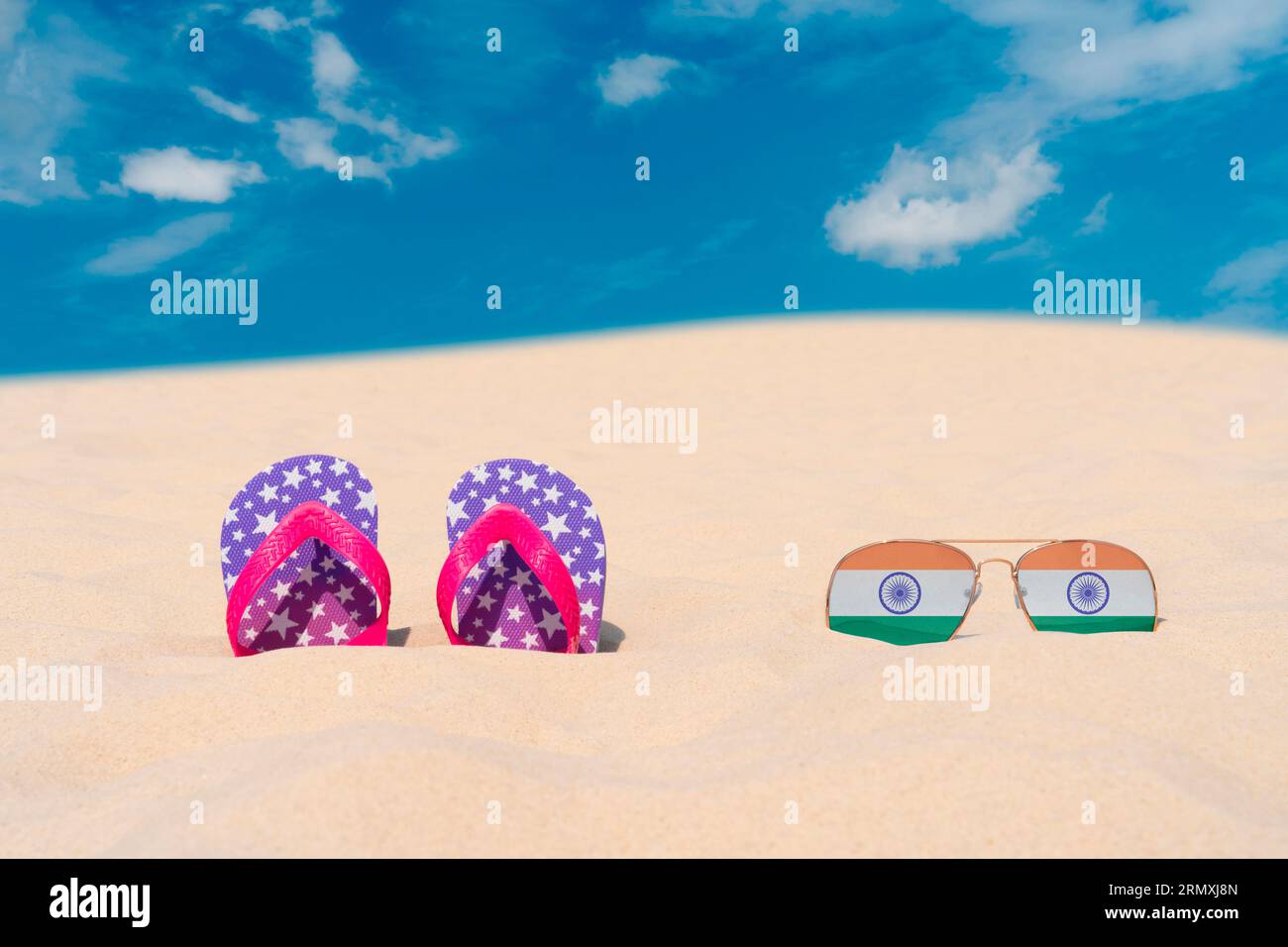 Sonnenbrillen mit Gläsern in Form einer indischen Flagge und Flip-Flops liegen auf Sand gegen blauen Himmel. Konzept von Sommerferien und Reisen in Indien Stockfoto