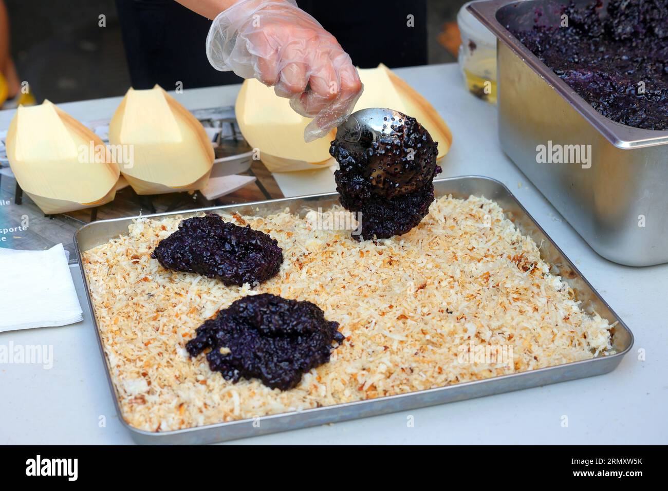 Eine Person, die Biko na Pirurutong zubereitet, einen philippinischen Dessertkuchen, der auf einem Straßenmarkt mit glutenfreiem schwarzen Reis und gebratenem Kokosmilchquark überzogen ist Stockfoto