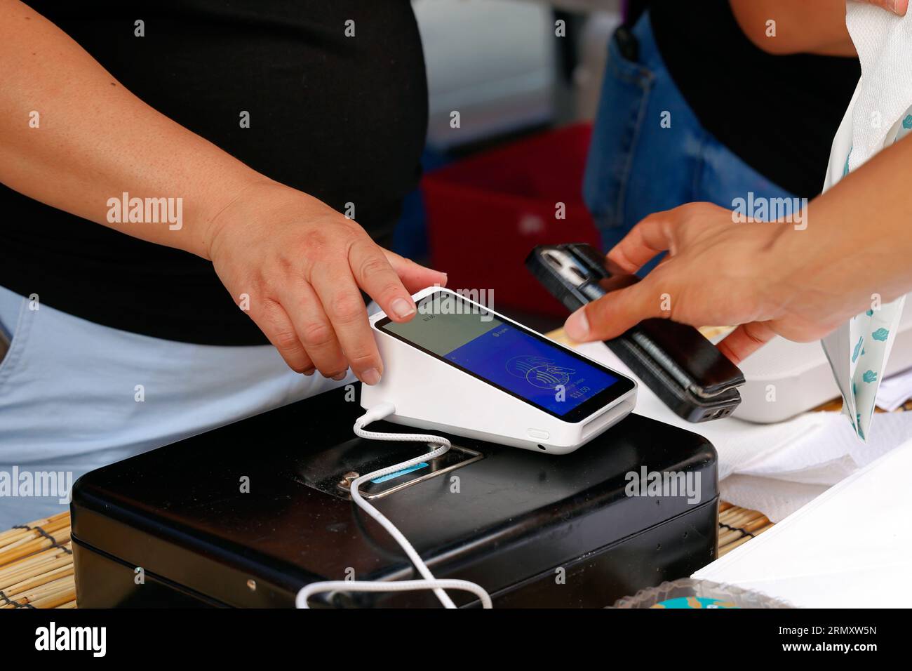 Eine Person hält ein Smartphone über ein drahtloses Square Terminal Point of Sales-Gerät, um eine NFC-mobile Zahlung oder kontaktlose digitale Zahlung zu tätigen. Stockfoto
