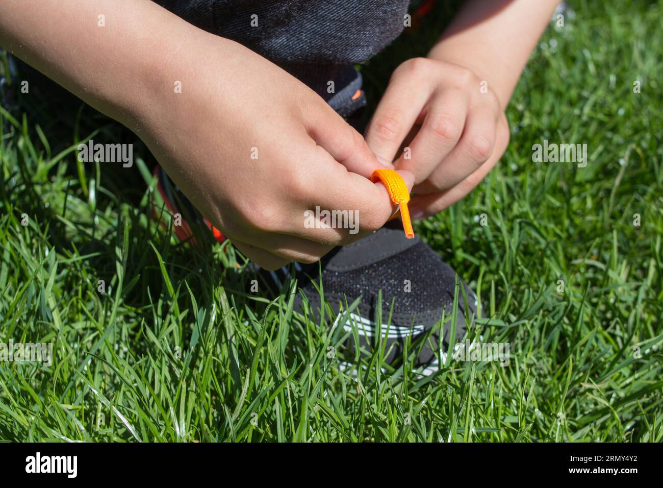 Lerne einen Jungen, die Schnürsenkel in den Sneakers auf dem Gras zu binden Stockfoto