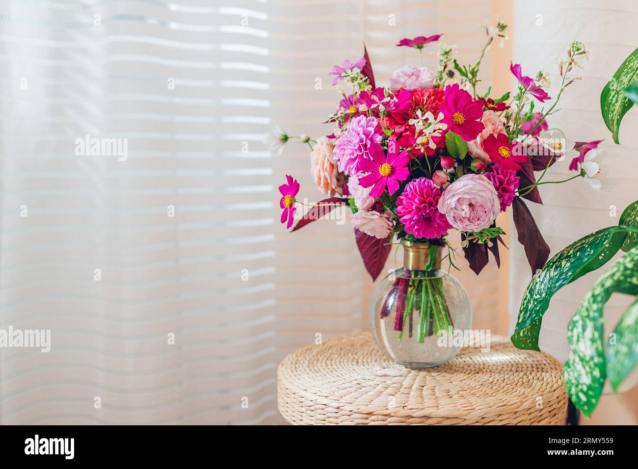 Nahaufnahme des Sommerstraußes von rosa Rosen Dahlien Blumen in Vase auf Strohrattan Korbpad. Inneneinrichtung und Einrichtung zu Hause. Leerzeichen Stockfoto