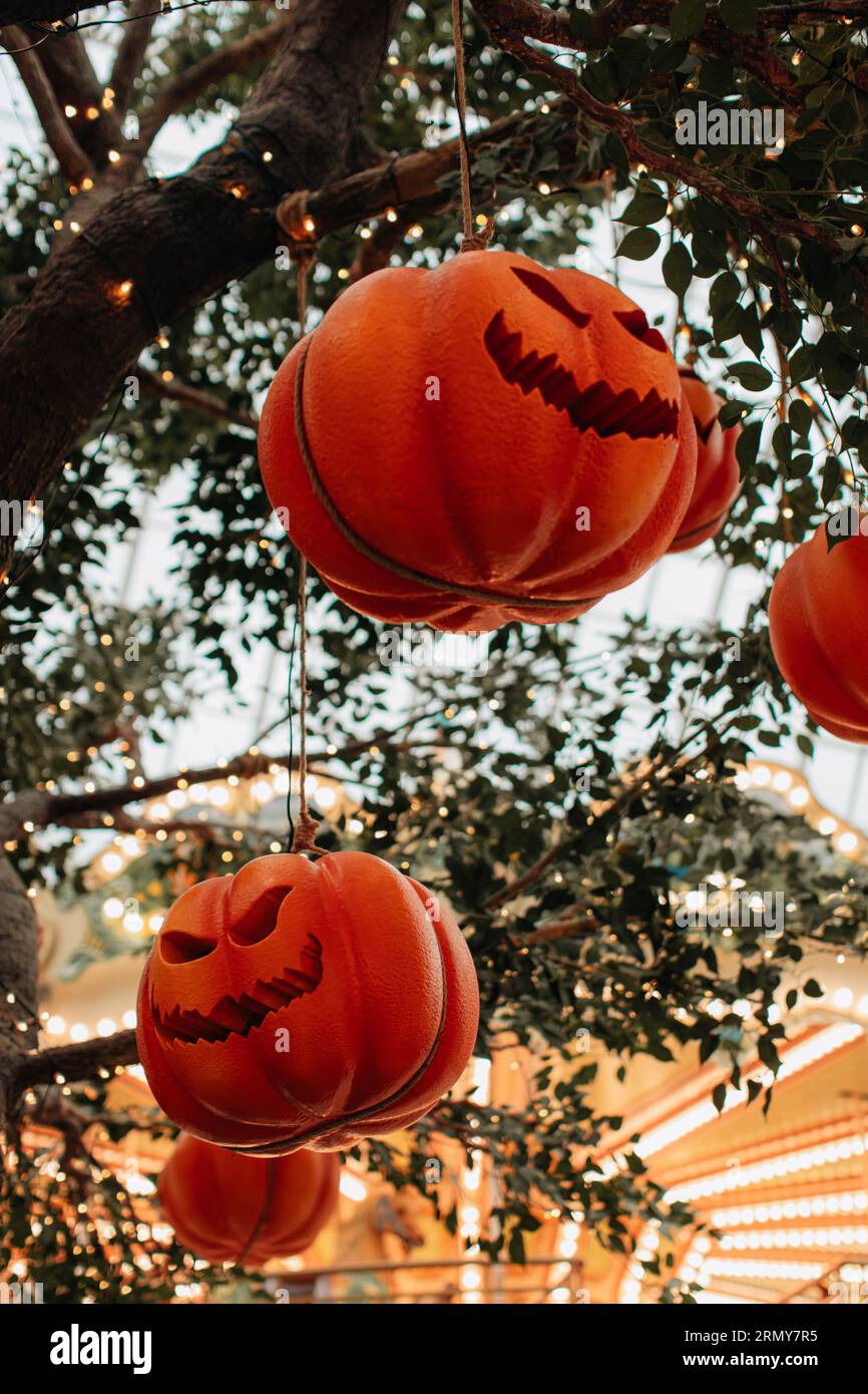Leuchtend oranger Kürbis mit einem gruseligen Halloween-Gesicht, das an einem Baum mit Girlanden hängt. Hintergrund für halloween-Party Stockfoto