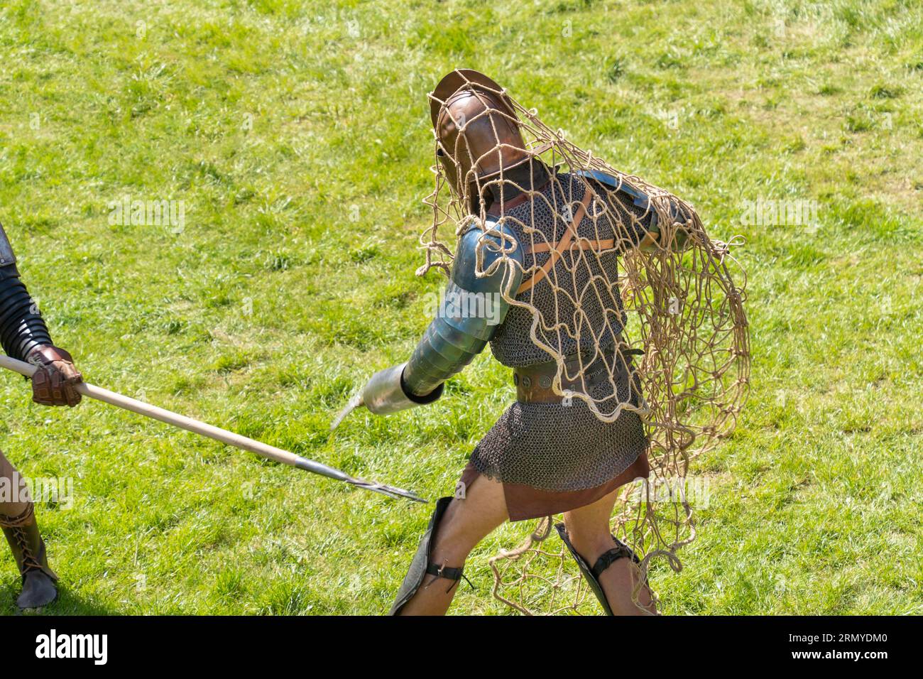 Ein römischer Gladiator, der sich in ein Netz verstrickt hat, kämpft auf einem grünen Grasfeld Stockfoto
