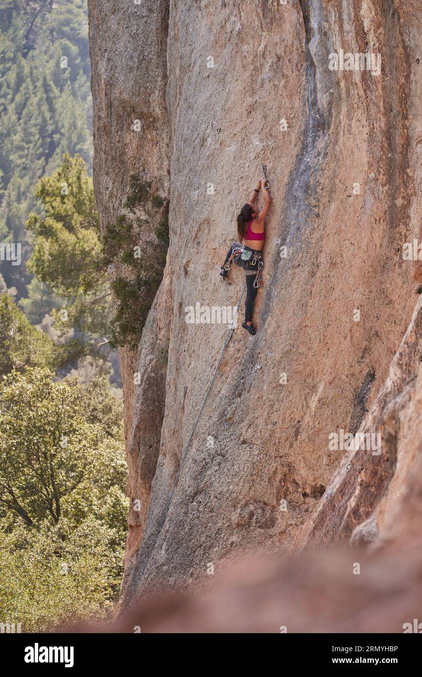 Rückansicht einer entfernten, nicht erkennbaren aktiven Bergsteigerin, die einen rauen felsigen Berghang mit Kletterausrüstung während des Trainings in der Natur erklimmt Stockfoto