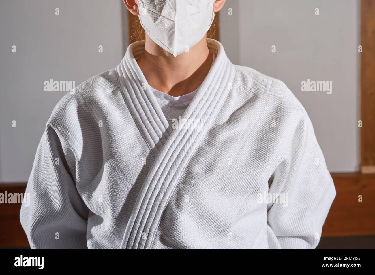 Nicht erkennbare Frau in medizinischer Maske, die Kimono trägt, der in einem hellen Raum während einer Pandemie steht Stockfoto