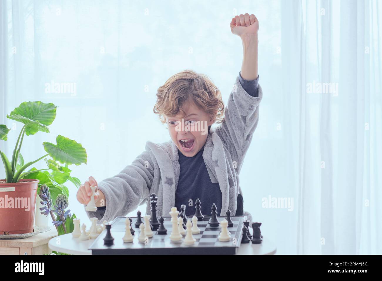 Glücklicher junger Junge, der Schachkamerad macht und mit erhobener Hand eine Faust-nach-oben-Geste zeigt, während er das Schachspiel gewinnt Stockfoto