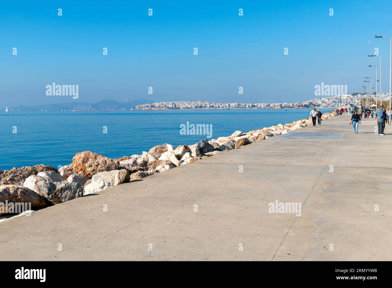 Die Fußgängerzone und Promenade am Meer entlang der Athenischen Riviera in der griechischen Stadt Palaio Faliro, mit Piräus Griechenland im Blick hinter. Stockfoto